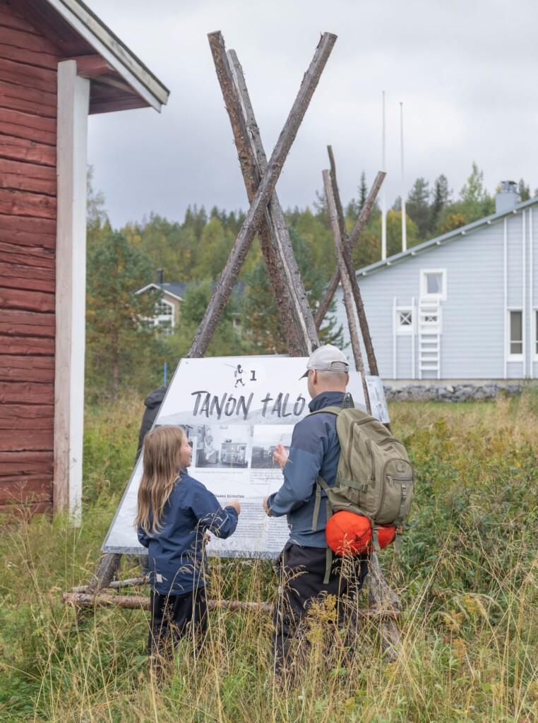 A child and an adult exploring the first stop of the Äkäslompolo storytelling trail, which tells the story of the Tano's house.