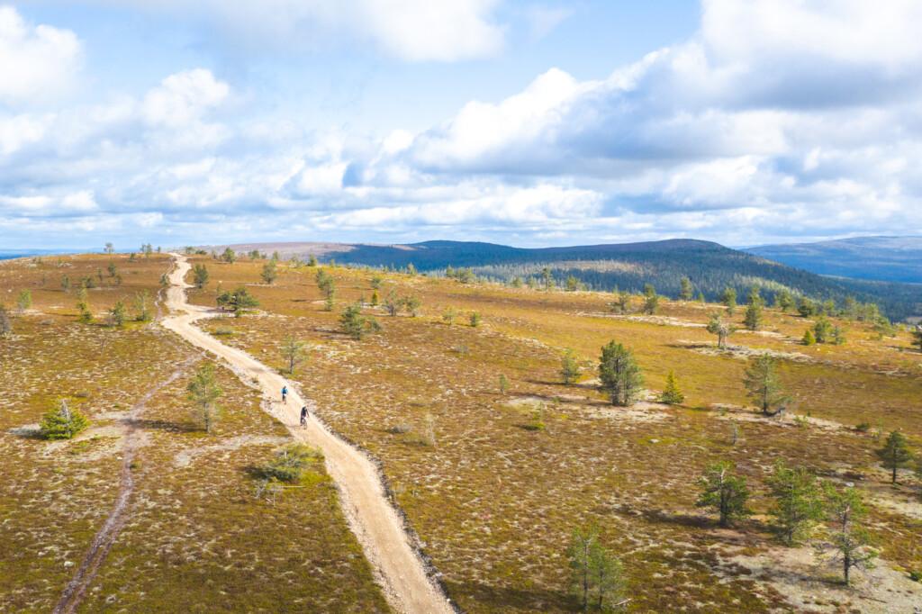 Aurinkoinen tunturin laki, jossa kulkee leveä sorapolku. Polulla on kaksi pyöräilijää. Taustalla sininen taivas jossa pilviä.