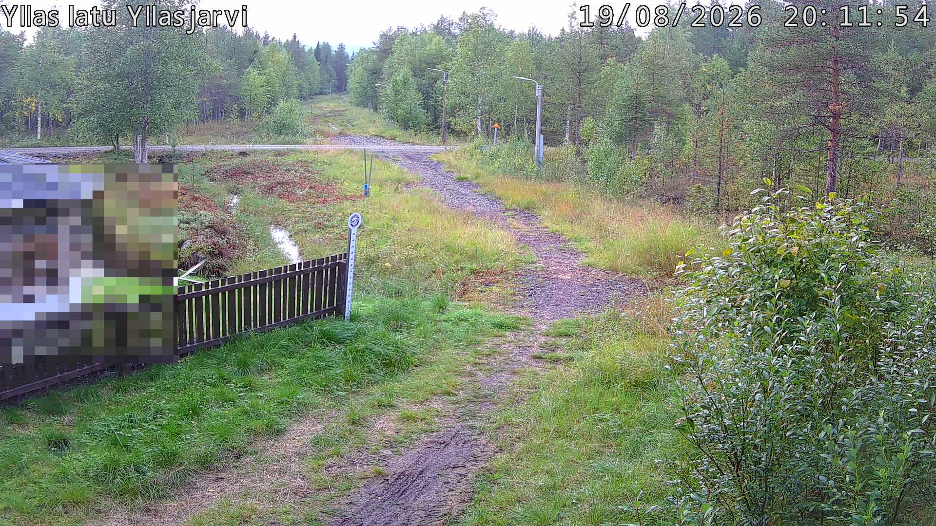 Talvella hieman mutkitteleva hiihtolatu, kesällä metsää, ja kauempana taustalla puiden yläpuolella hieman Yllästunturin rinnettä.