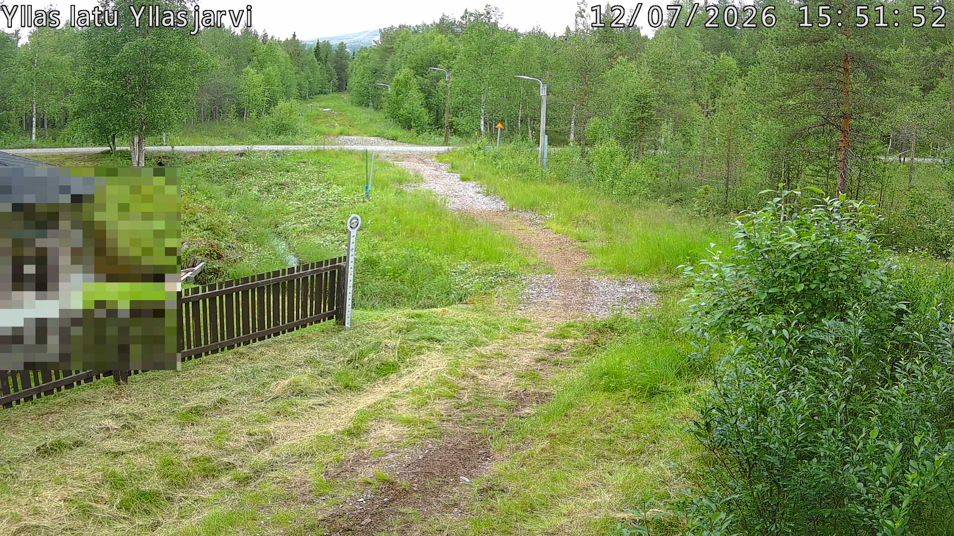Talvella hieman mutkitteleva hiihtolatu, kesällä metsää, ja kauempana taustalla puiden yläpuolella hieman Yllästunturin rinnettä.