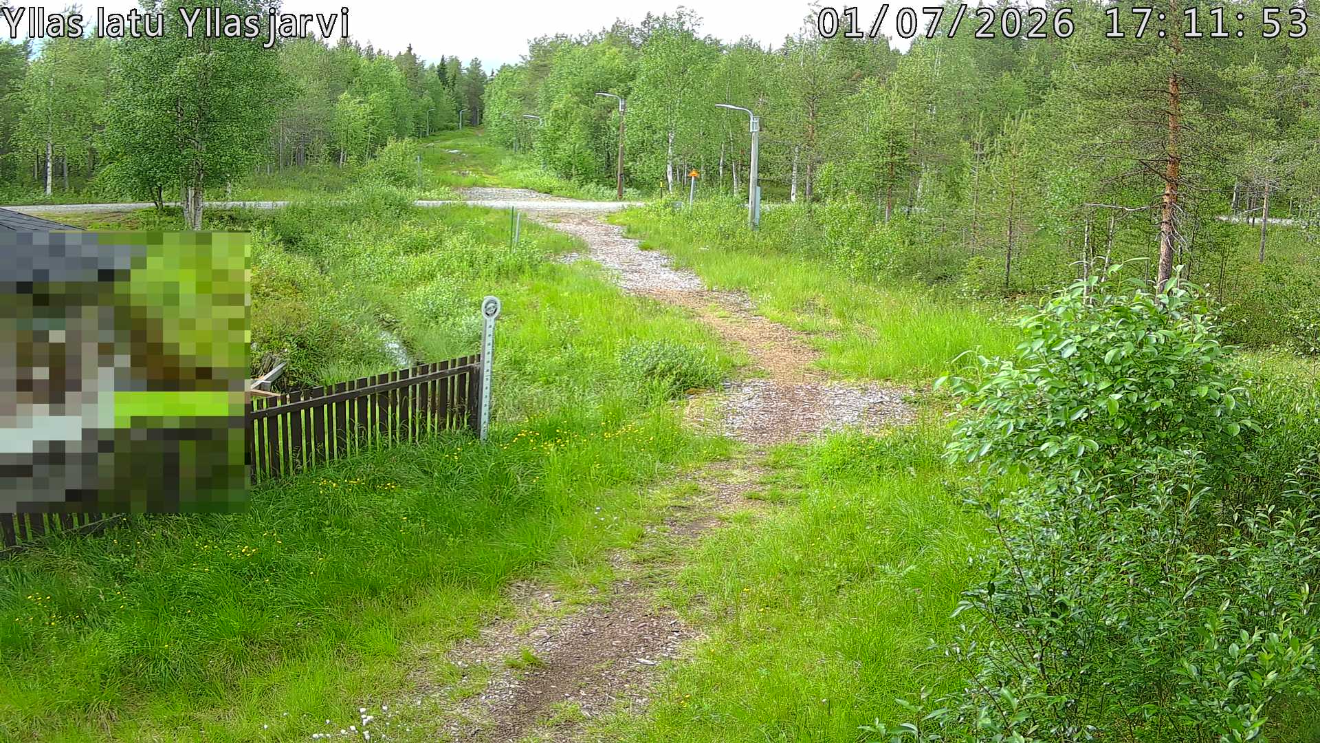 Talvella hieman mutkitteleva hiihtolatu, kesällä metsää, ja kauempana taustalla puiden yläpuolella hieman Yllästunturin rinnettä.
