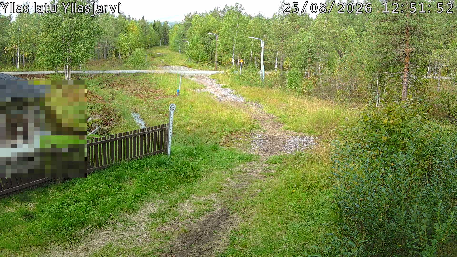 Talvella hieman mutkitteleva hiihtolatu, kesällä metsää, ja kauempana taustalla puiden yläpuolella hieman Yllästunturin rinnettä.