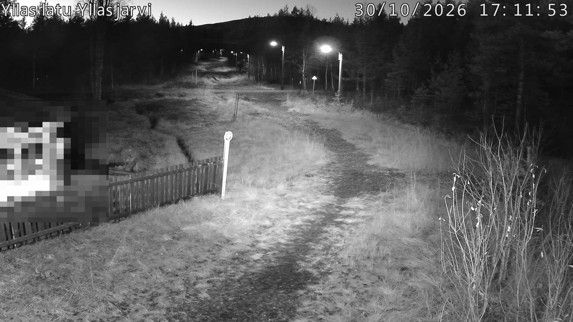 Talvella hieman mutkitteleva hiihtolatu, kesällä metsää, ja kauempana taustalla puiden yläpuolella hieman Yllästunturin rinnettä.