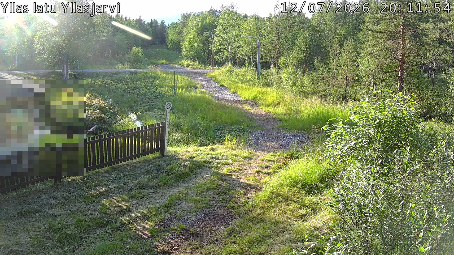 Talvella hieman mutkitteleva hiihtolatu, kesällä metsää, ja kauempana taustalla puiden yläpuolella hieman Yllästunturin rinnettä.