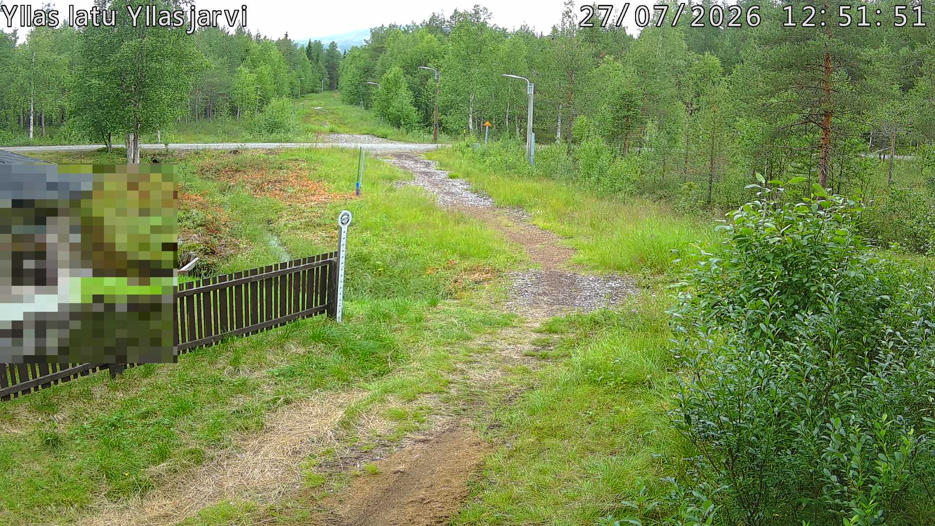 Talvella hieman mutkitteleva hiihtolatu, kesällä metsää, ja kauempana taustalla puiden yläpuolella hieman Yllästunturin rinnettä.