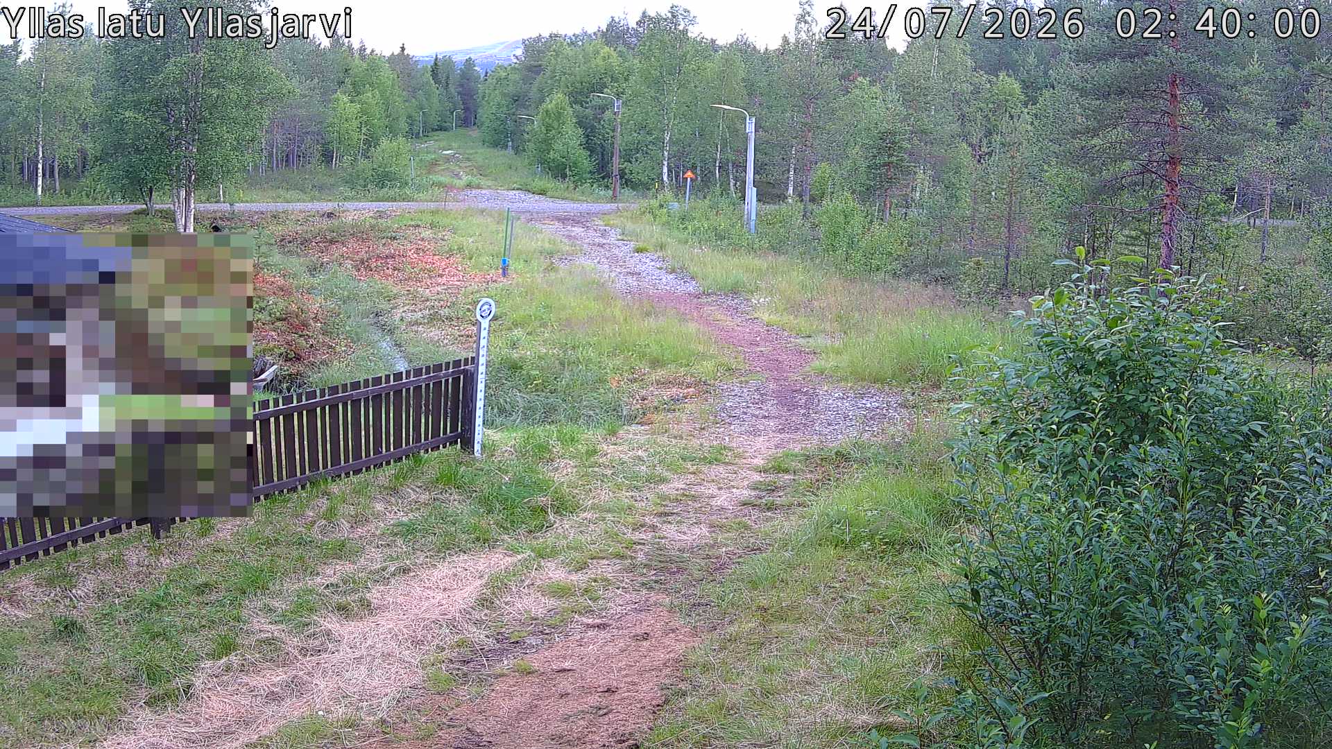 Talvella hieman mutkitteleva hiihtolatu, kesällä metsää, ja kauempana taustalla puiden yläpuolella hieman Yllästunturin rinnettä.