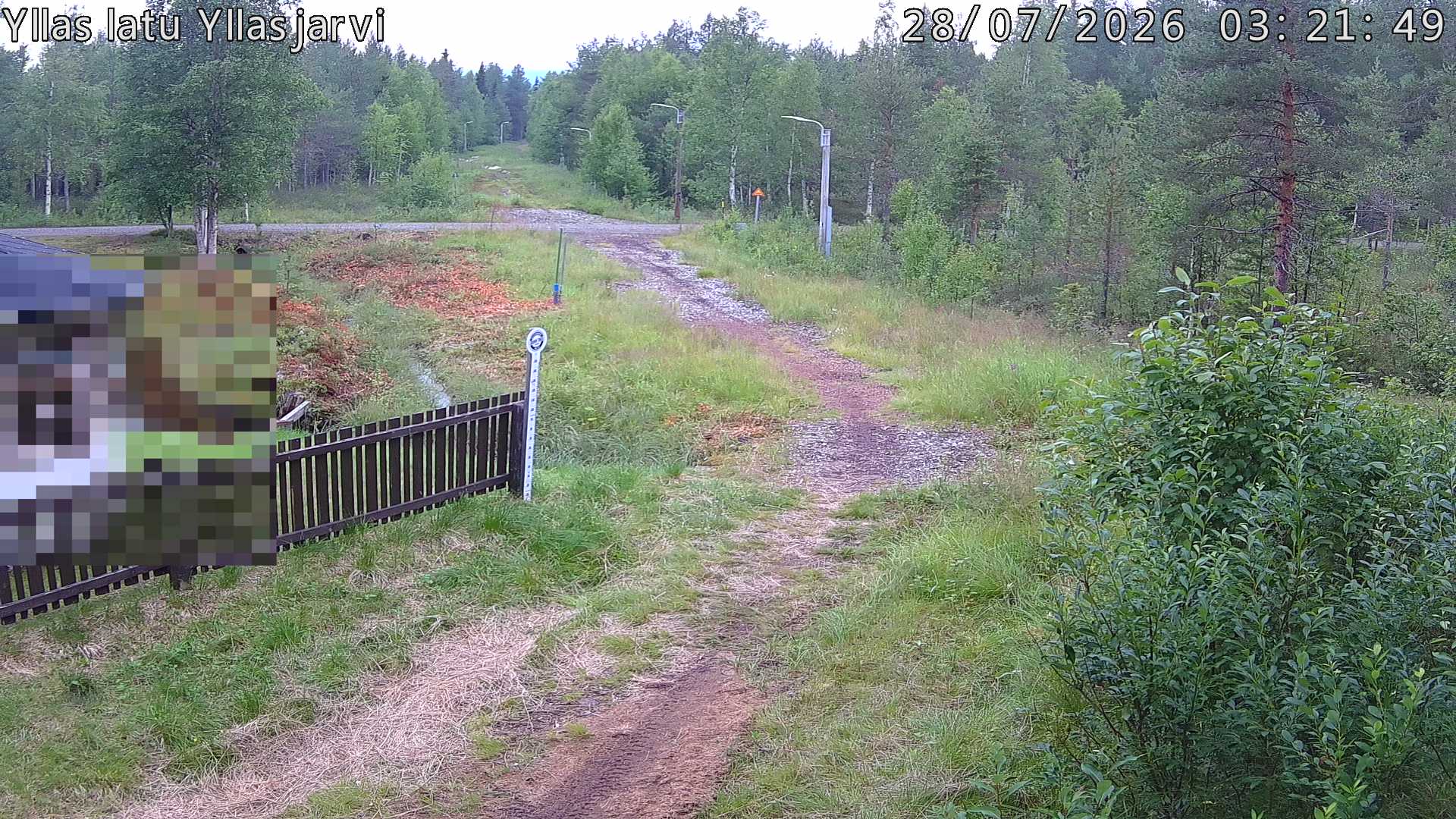 Talvella hieman mutkitteleva hiihtolatu, kesällä metsää, ja kauempana taustalla puiden yläpuolella hieman Yllästunturin rinnettä.