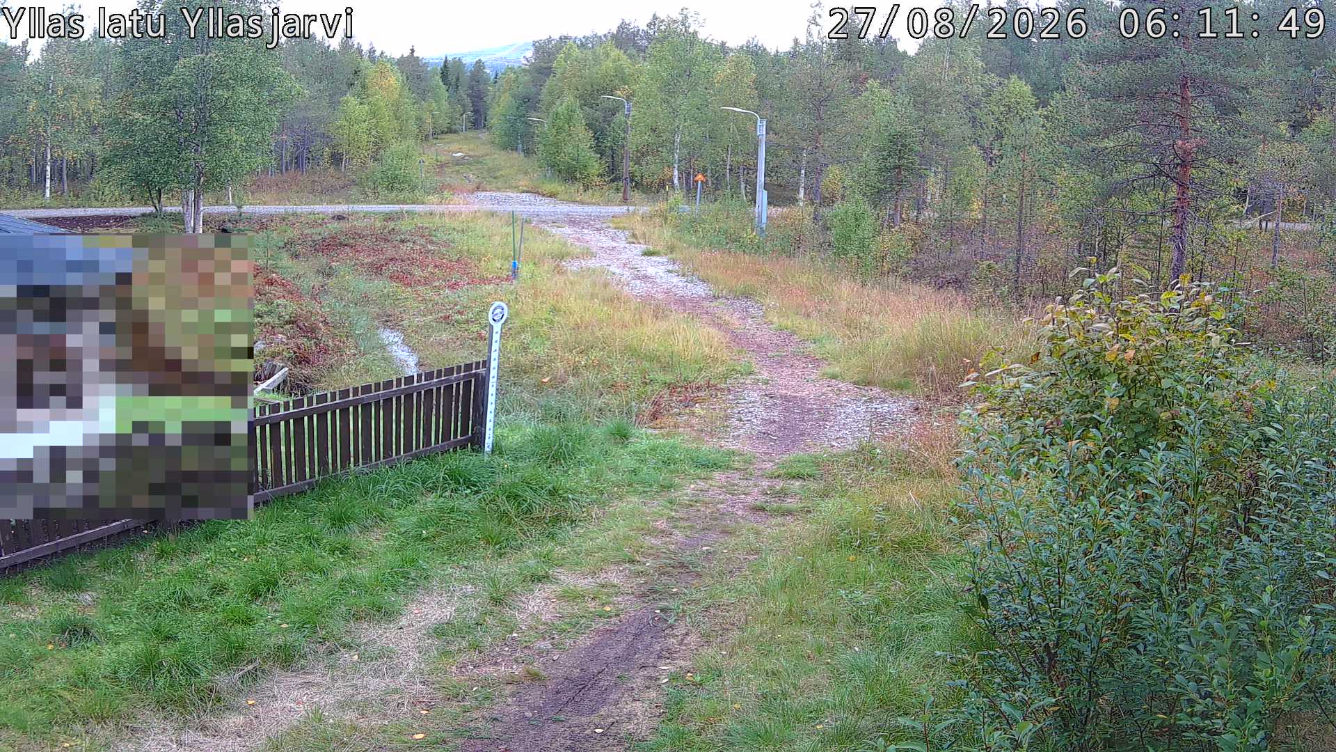Talvella hieman mutkitteleva hiihtolatu, kesällä metsää, ja kauempana taustalla puiden yläpuolella hieman Yllästunturin rinnettä.