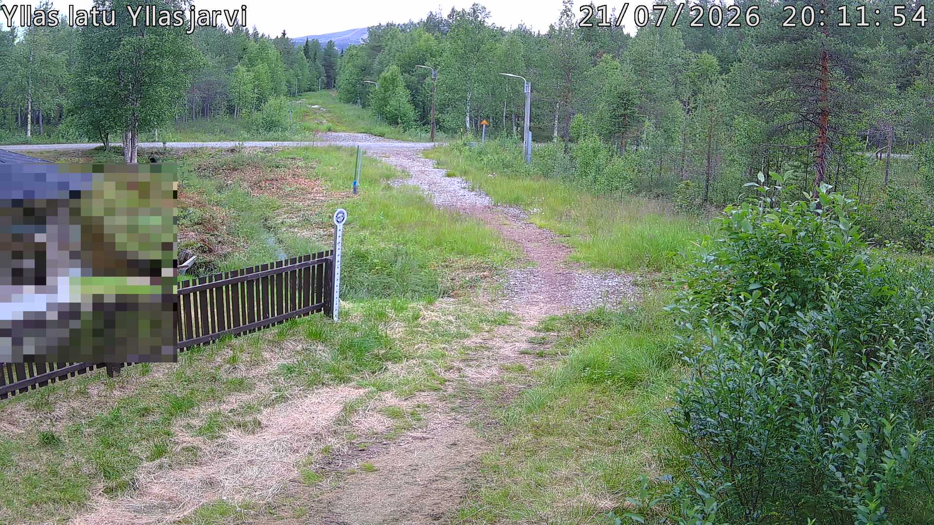 Talvella hieman mutkitteleva hiihtolatu, kesällä metsää, ja kauempana taustalla puiden yläpuolella hieman Yllästunturin rinnettä.